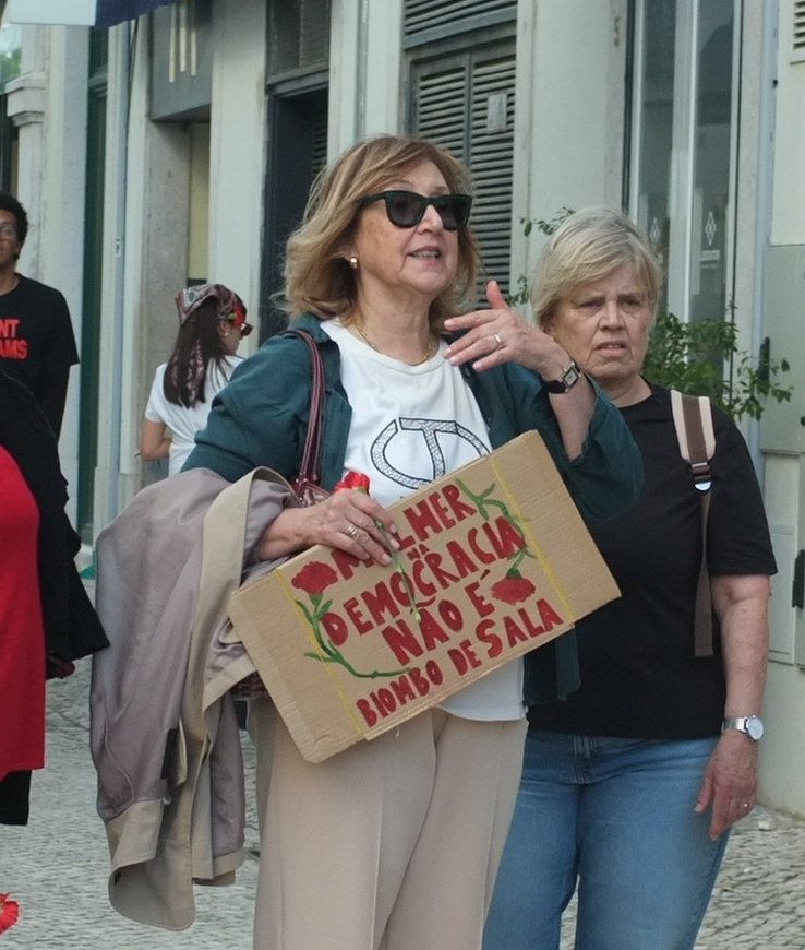 Uma senhora com uma certa idade segura um cartaz que diz "Mulher em Democracia não é biombo de sala", numa referência a uma letra do Zeca Afonso