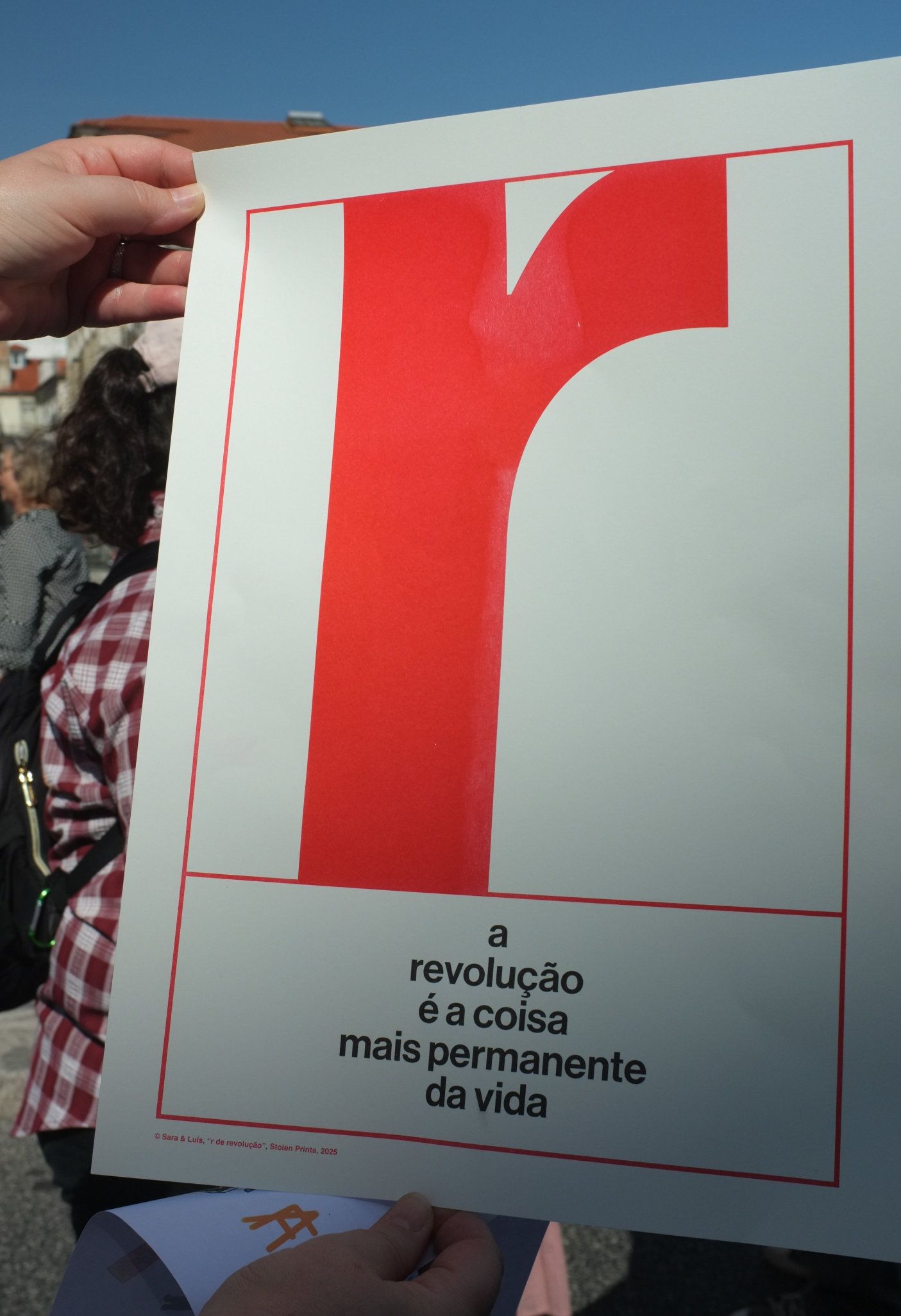 Um cartaz com um R maíusculo e grande e a frase "A Revolução É a Coisa Mais Permanente da Vida"