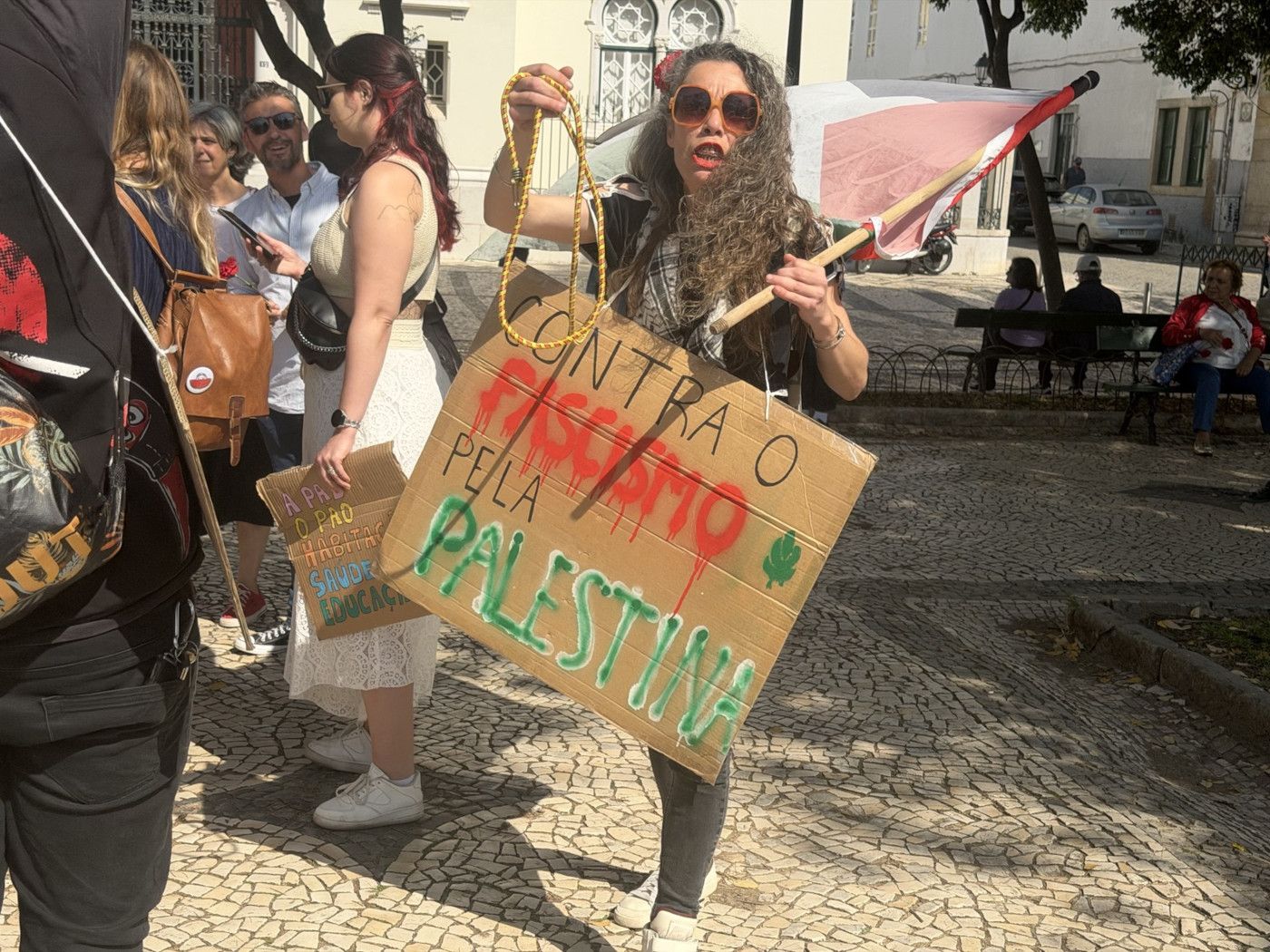 Mulher de óculos e com bandeira da Palestina com a seguinte descrição