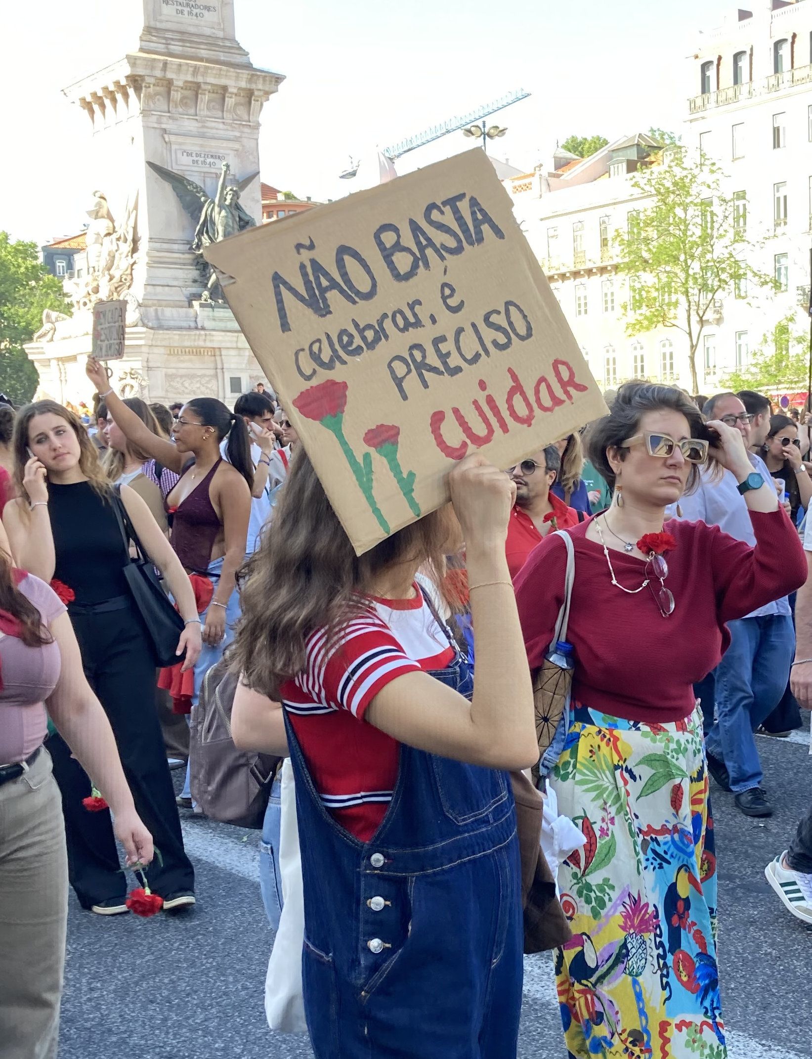 Uma rapariga segura um cartaz que diz "Não Basta Celebrar, É Preciso Cuidar"