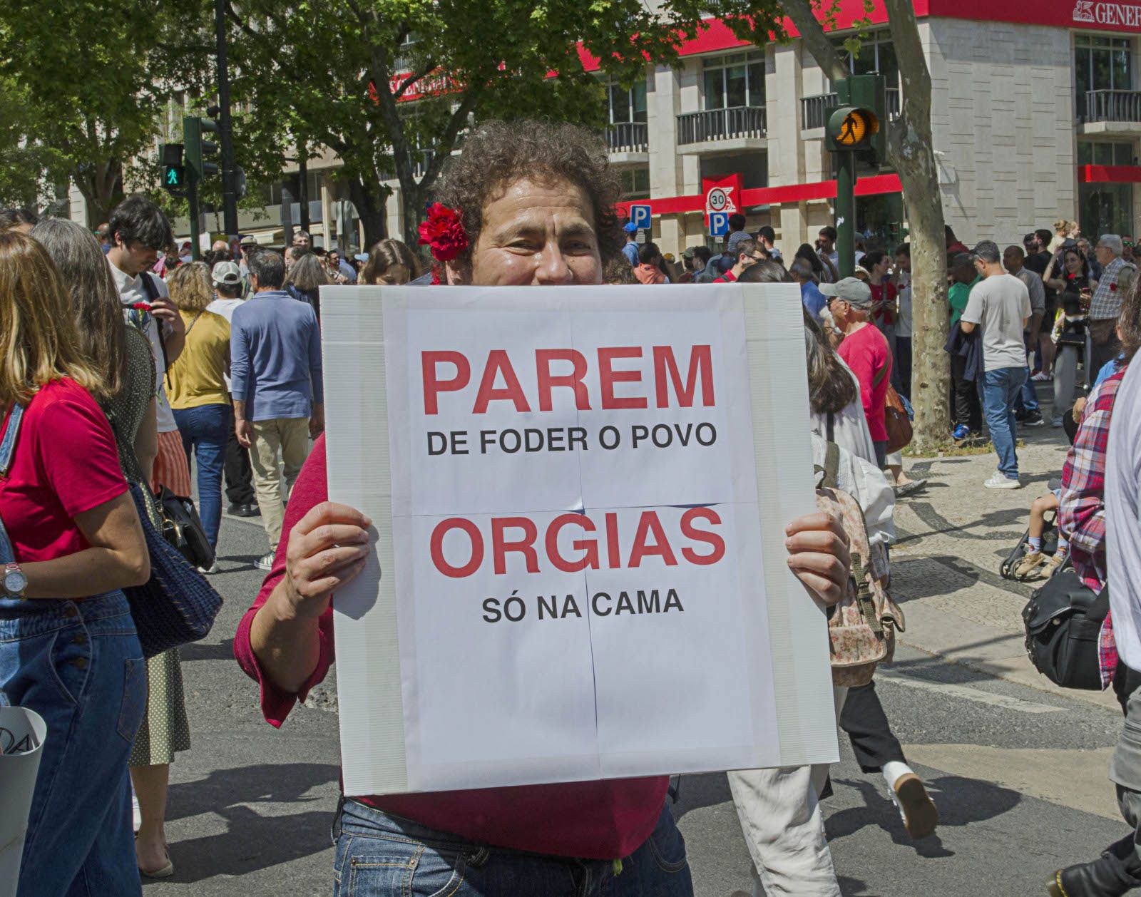 Um pessoa com um cravo na orelha, e no meio da manifestação segura um cartaz onde se lê "Parem de foder o povo, orgias só na cama".